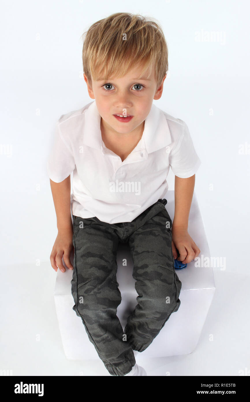 Adorable muchacho sentado en un cubo gigante de papel y elevando su cabeza hacia arriba Foto de stock