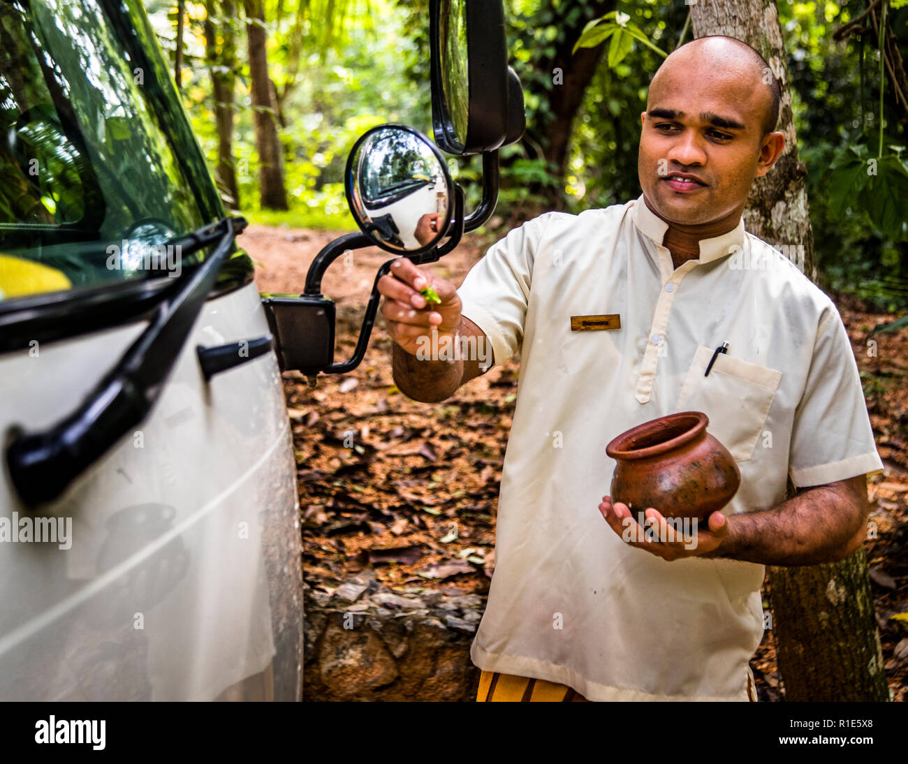 Ritual de despedida en Sri Lanka. Bendiciones budistas para un viaje seguro. Mientras las maletas están siendo cargadas en la parte de atrás, el gerente del hotel rocía agua con pétalos de flores en la parte delantera del vehículo. Con esto se debe alcanzar el siguiente objetivo de forma segura Foto de stock