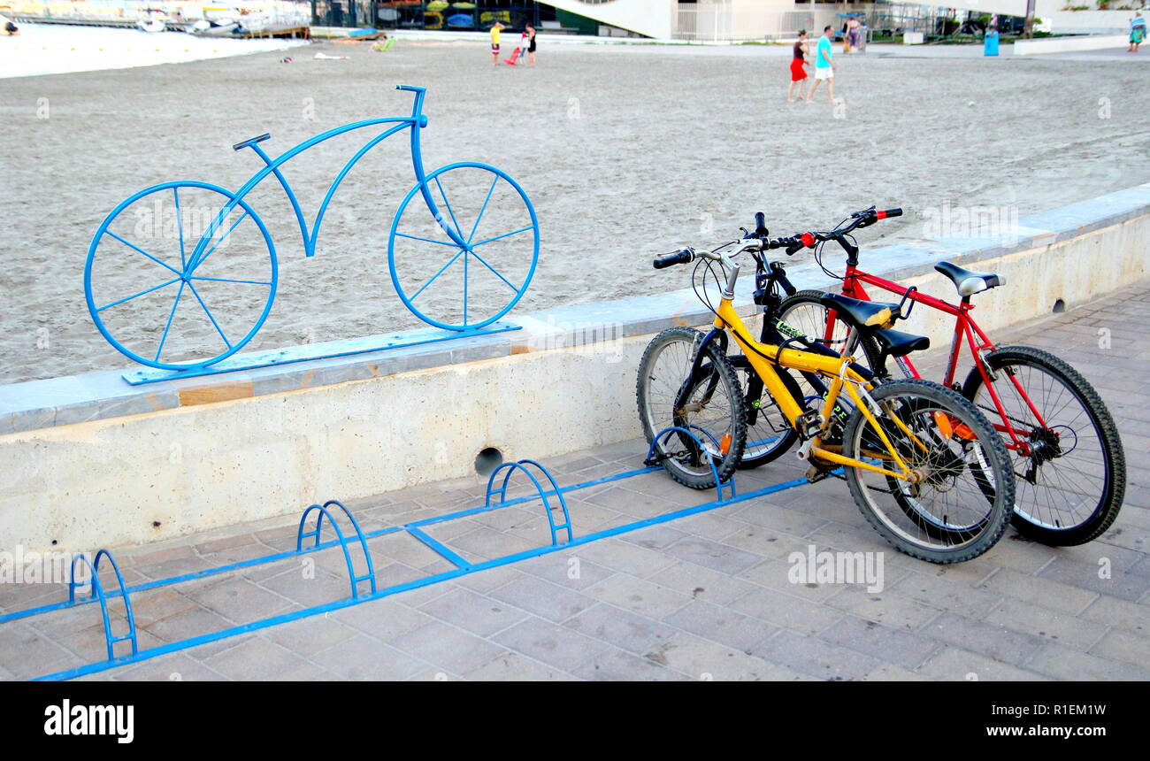 Santiago de la Ribera, Murcia, España - 31 de julio 2018: Bicicletas  aparcado en un portabicicletas, caracterizado por una moderna escultura en  hierro forjado de una bicicleta, con el Fotografía de stock - Alamy