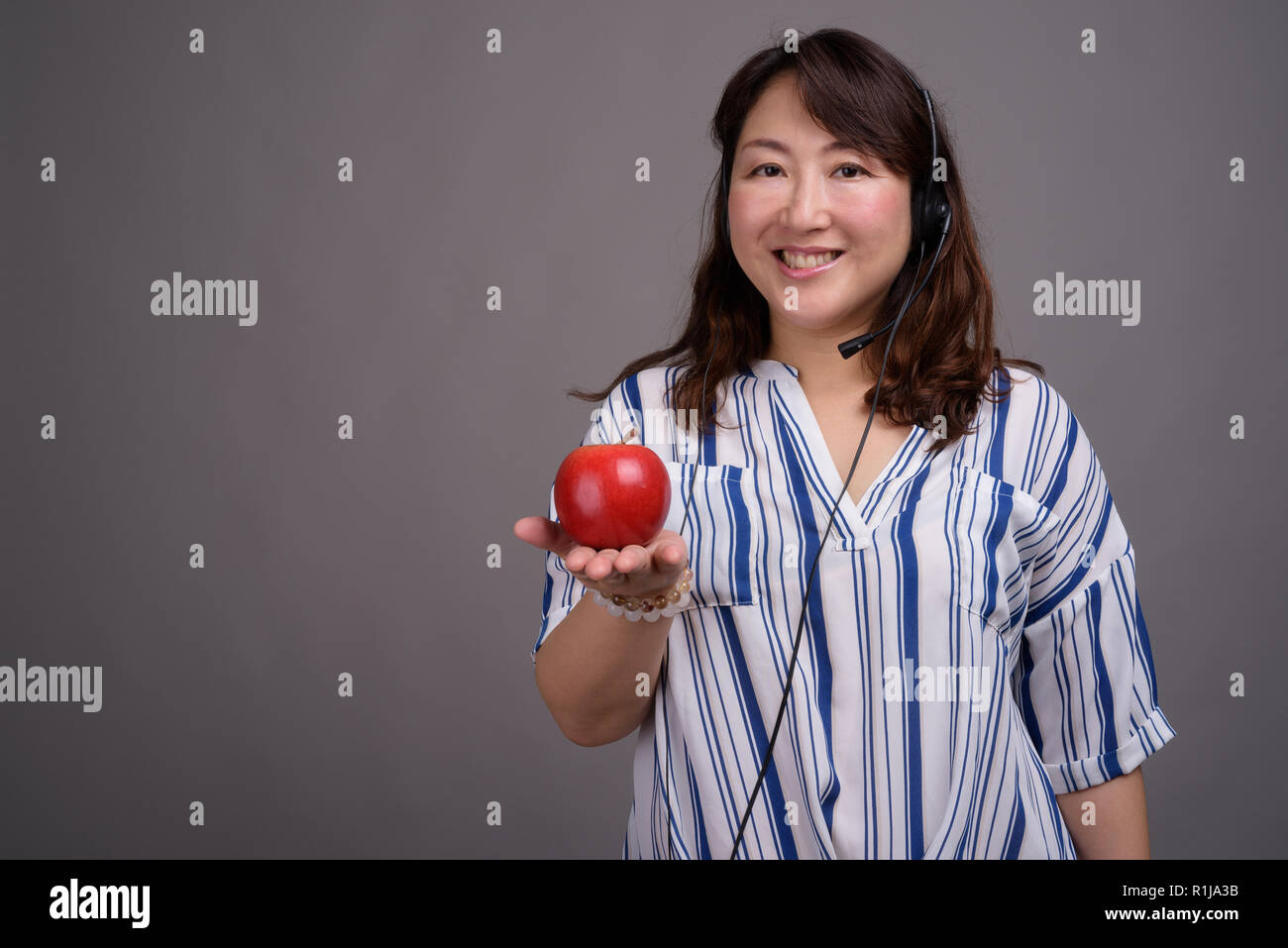 El representante del centro de llamadas asiáticos madura mujer sosteniendo apple Foto de stock