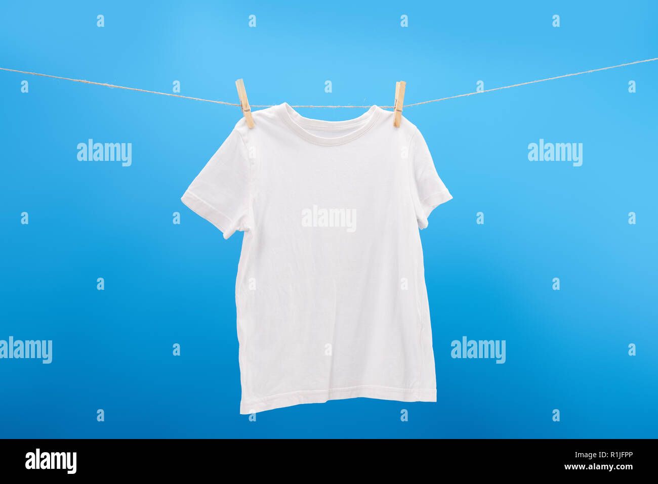 Camiseta blanca con broches colgando en el tendedero aislado en azul  Fotografía de stock - Alamy