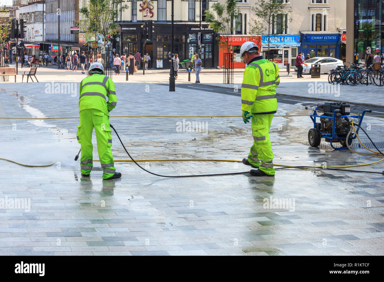 Limpiadores de calle con mangueras de presión en la plaza 'navegador', quitar la goma de mascar desde el nuevo centro peatonal de Arco, en el norte de Londres, Reino Unido Foto de stock
