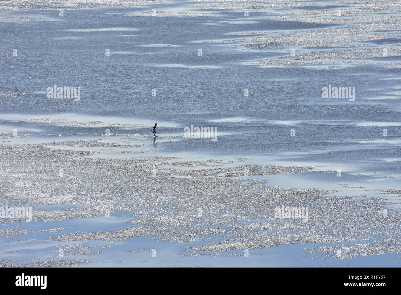 Diminuta figura de niño corriendo en la inmensa marea baja Sandy flats bañarse en luz plateada. Foto de stock
