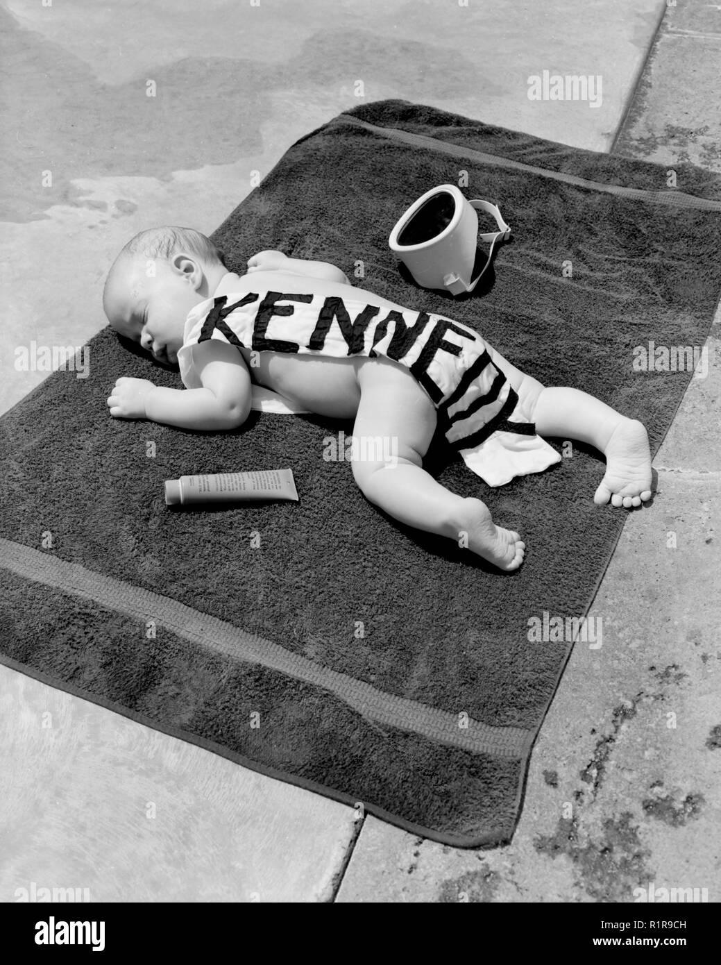 Un bebé con una guillotina Kennedy está al lado de la piscina, ca. 1960. Foto de stock
