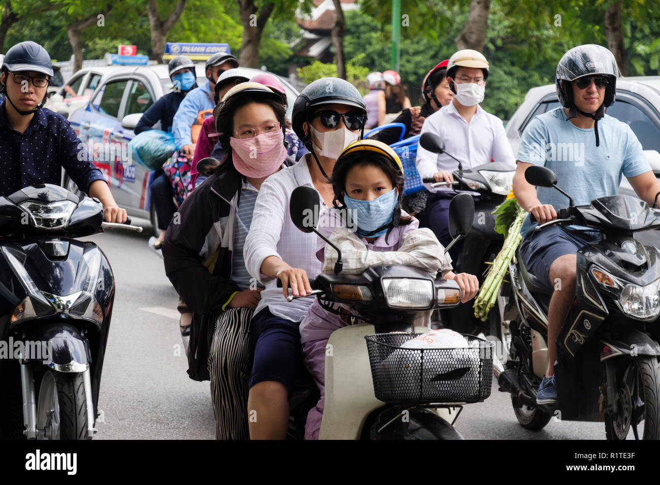 Escena callejera con personas vestidas con máscaras en motocicletas y scooters para proteger contra la contaminación del aire urbano en una concurrida calle. Hanoi, Vietnam, Asia Foto de stock