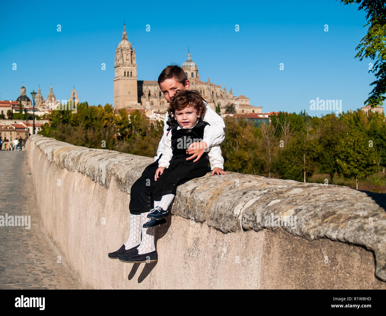 Dos niños hermanos sobre el Puente Romano de Salamanca, vestidos con ropas tradicionales Foto de stock