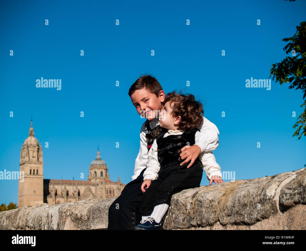 Dos niños hermanos abrazados sobre el Puente Romano de Salamanca, vestidos con ropas tradicionales y de la catedral de Salamanca Foto de stock