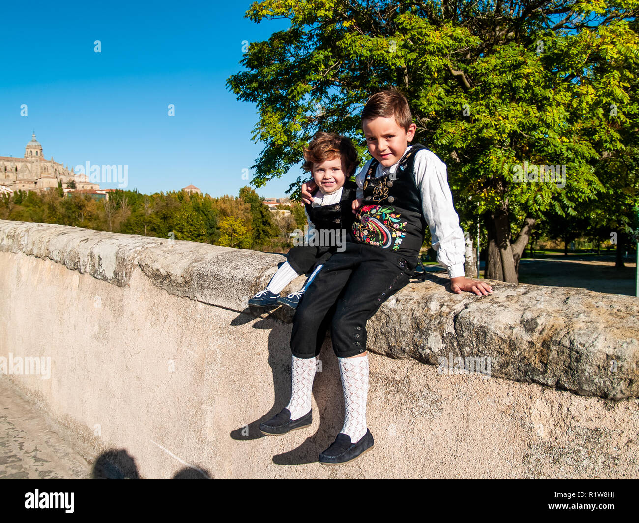 Dos niños hermanos abrazados sobre el Puente Romano de Salamanca, vestidos con ropas tradicionales Foto de stock