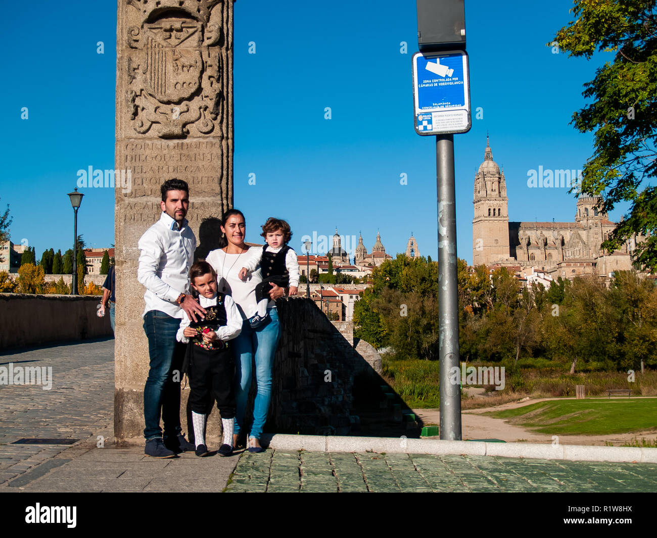 Una familia que viajaba con dos niños hermanos abrazados sobre el Puente Romano de Salamanca, vestidos con ropas tradicionales y de la catedral de Salamanca Foto de stock