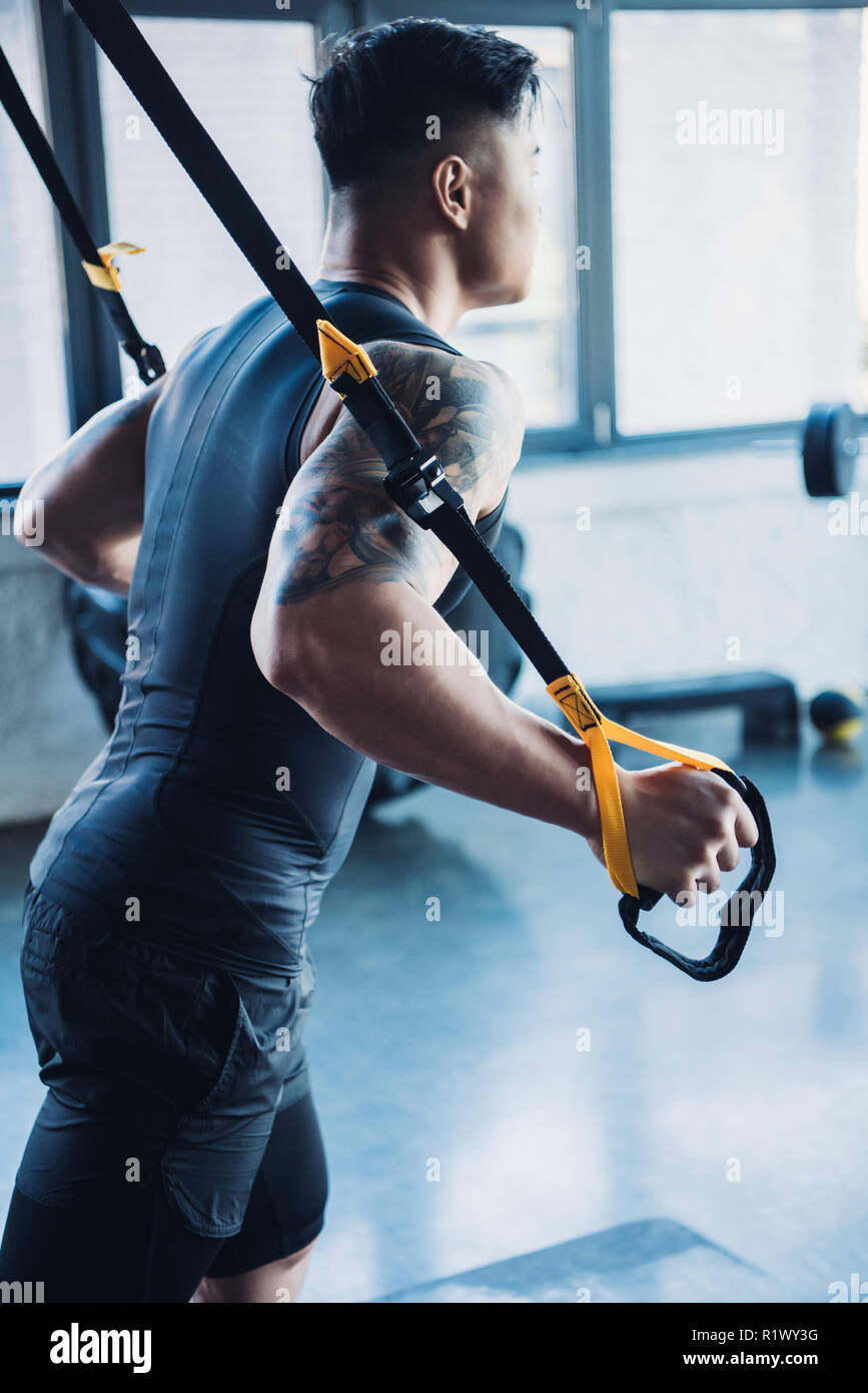 Vista lateral del joven deportista entrenamiento muscular con bandas de resistencia en el gimnasio Foto de stock