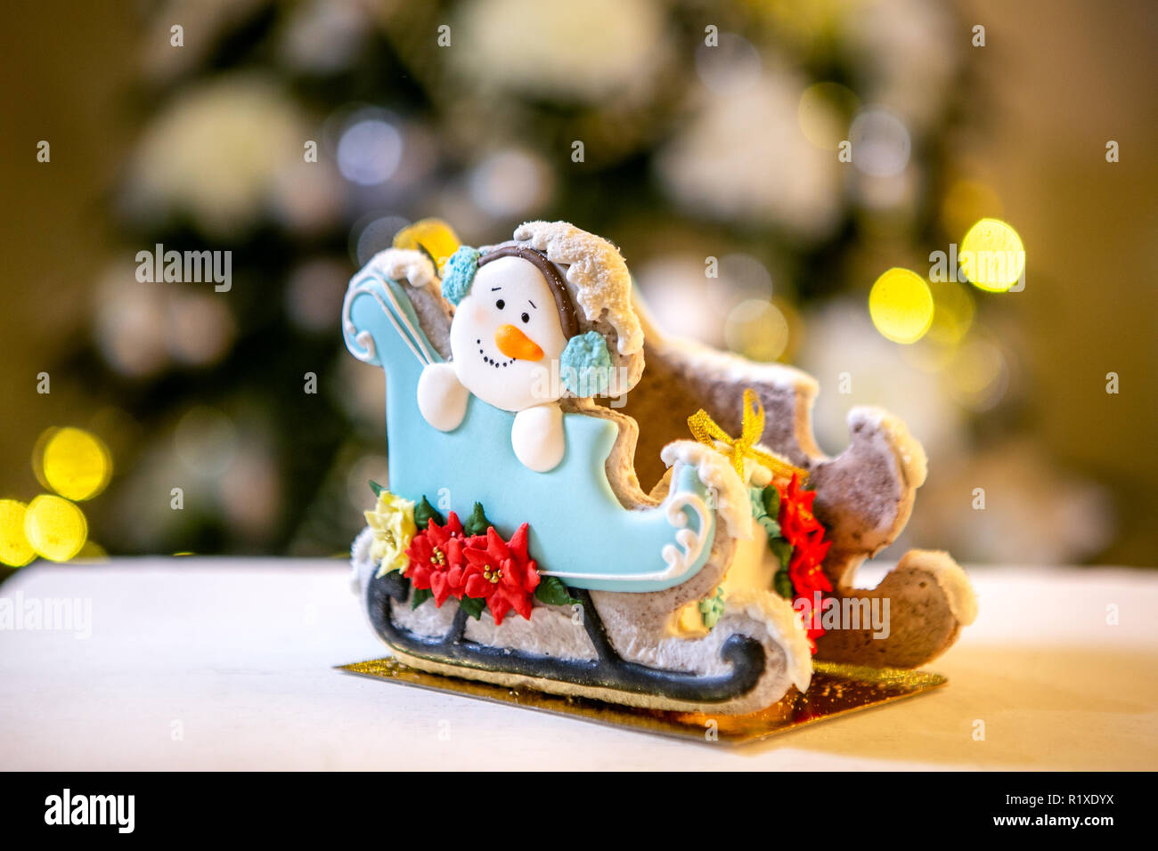 Gingerbread trineo con muñeco de nieve en la parte delantera de desenfoque luces de Navidad adornado abeto. Vacaciones dulces. Tema de Navidad y Año Nuevo. Mo festivo Foto de stock