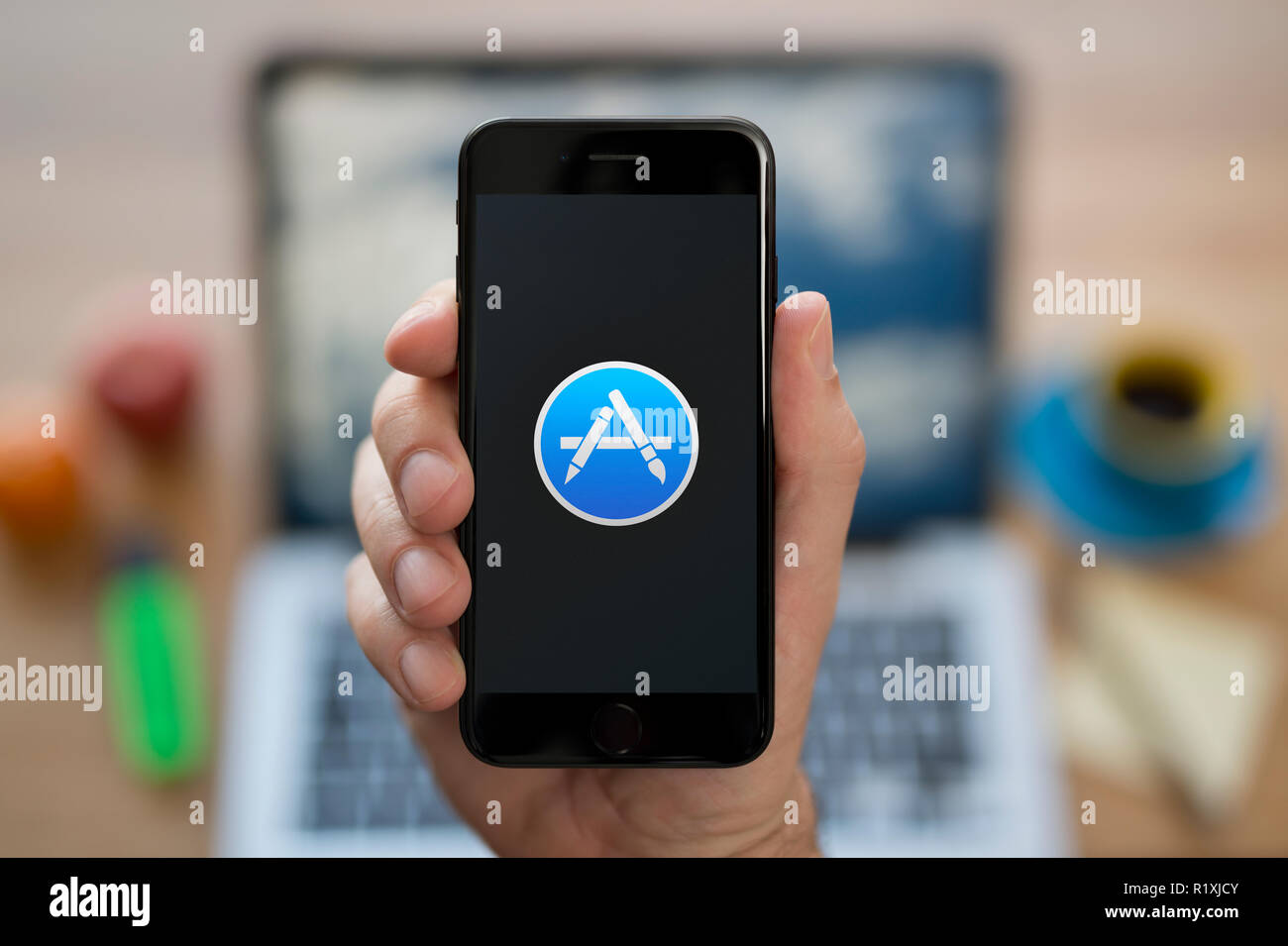 Un hombre mira el iPhone que muestra el logotipo de App Store, mientras estaba sentado en su escritorio de ordenador (uso Editorial solamente). Foto de stock