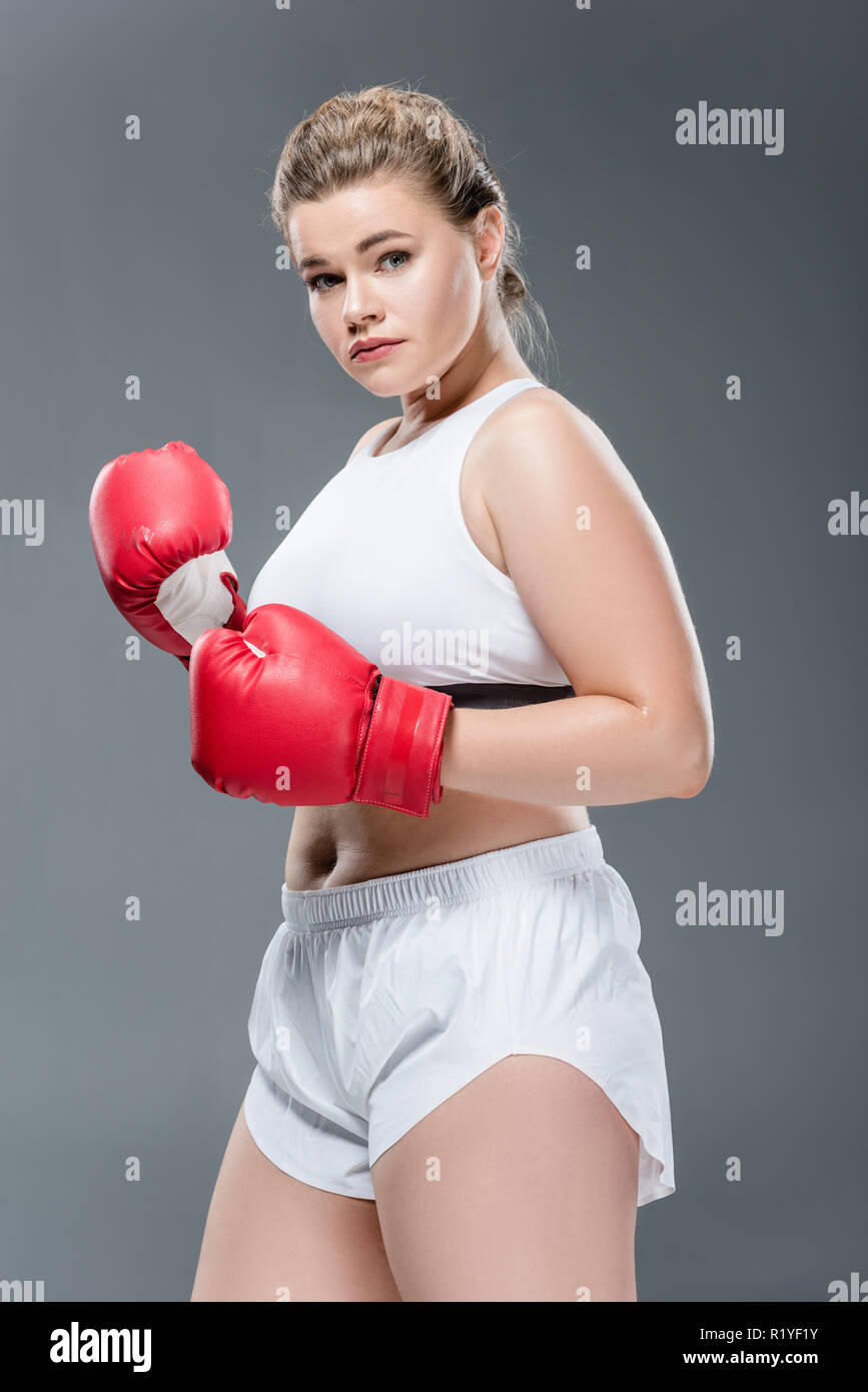 Tamaño de la joven mujer plus en ropa y guantes de boxeo mirando a la  cámara aislada sobre gris Fotografía de stock - Alamy
