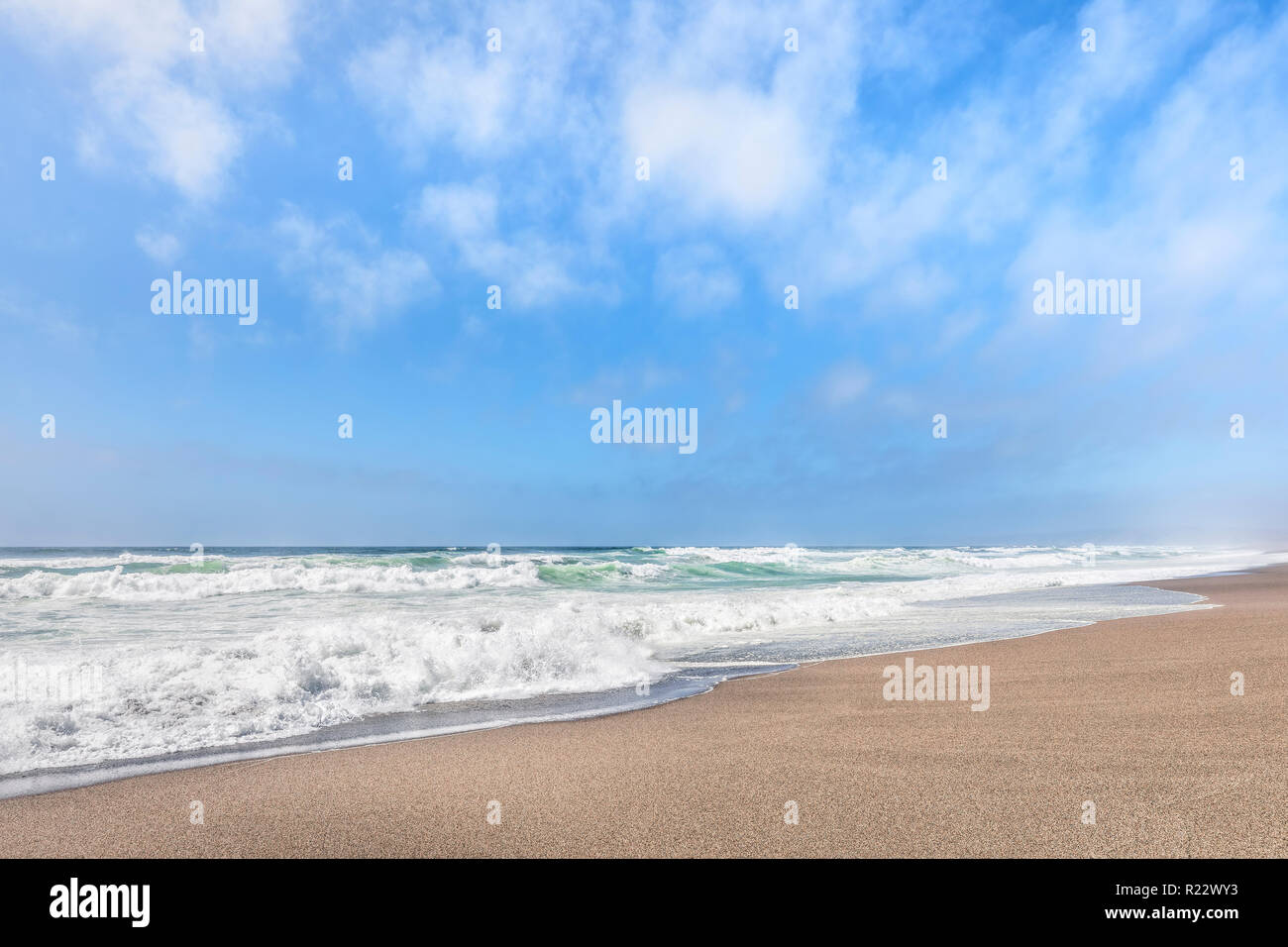 Suaves olas que rompen en una playa de arena, bajo un nublado cielo de verano azul a lo largo de California's Point Reyes National Seashore. Foto de stock
