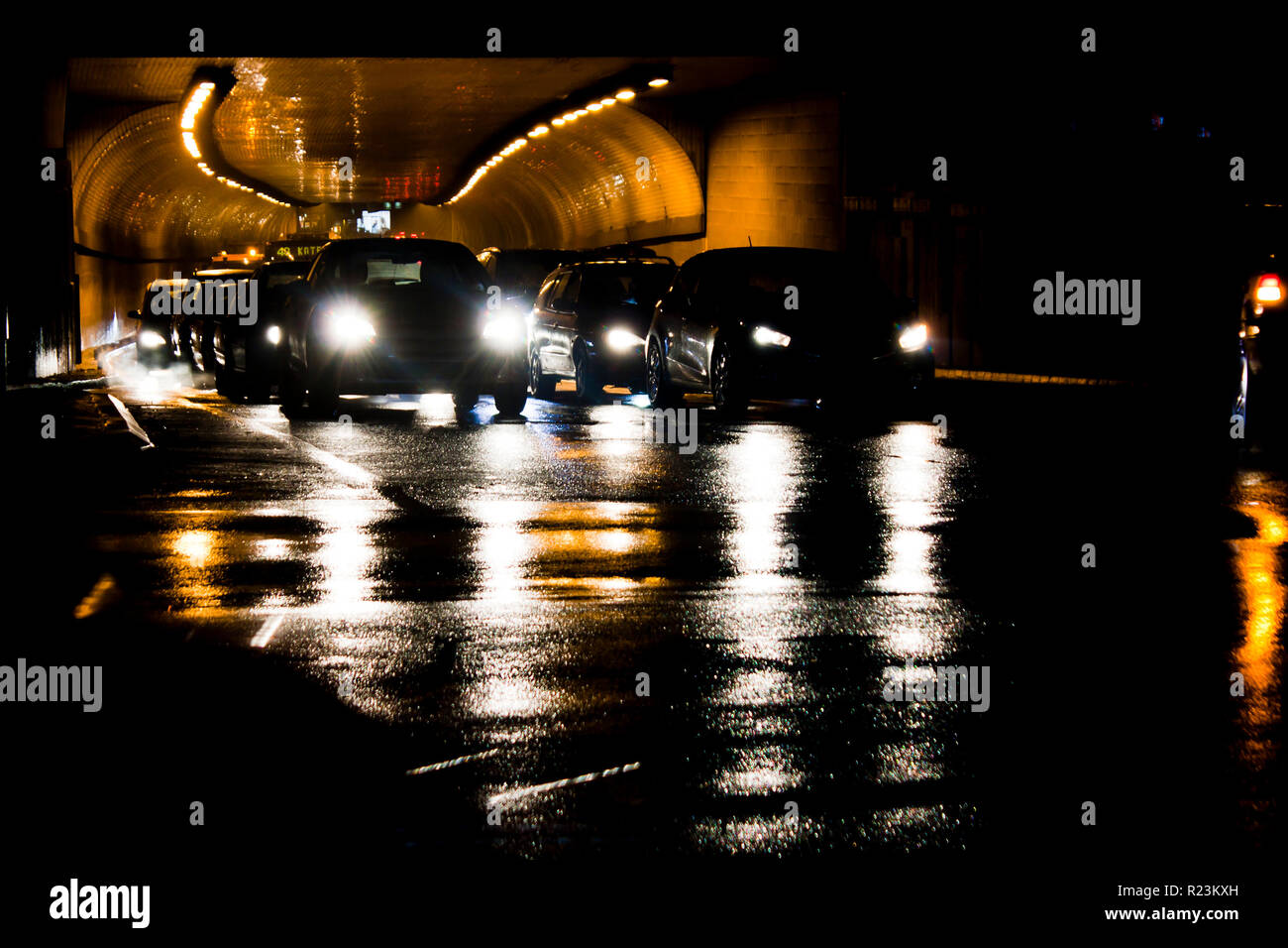 Tráfico nocturno en las calles de la ciudad de lluvia. Coches en cola de espera a la salida del túnel en la intersección durante la conducción de vehículos en movimiento pasado dejando estelas de luz de color Foto de stock