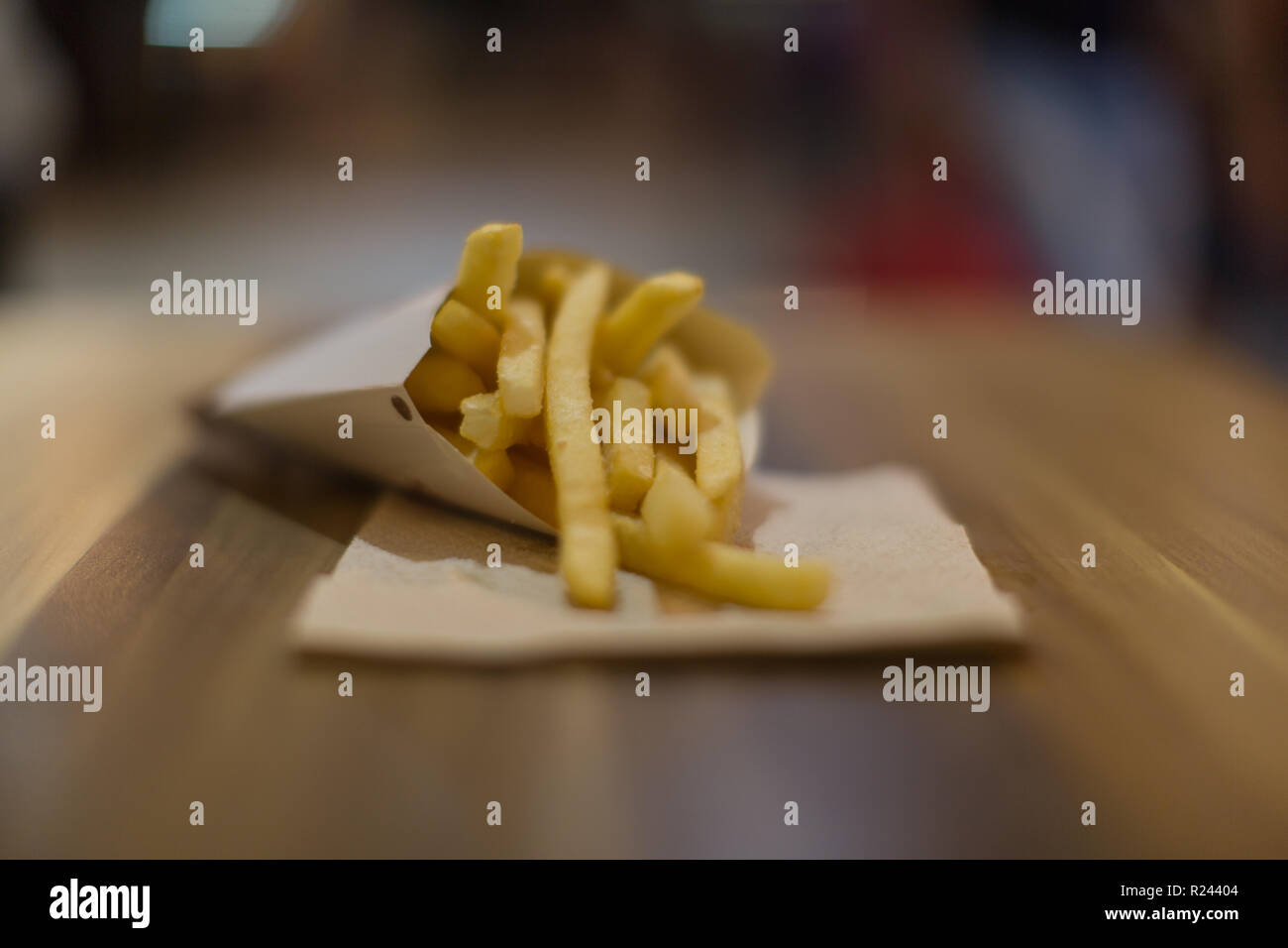 Patatas fritas appetizingly en cono de papel sobre una mesa de madera con fondo fuera de foco luces borrosa un bonito bokeh Foto de stock