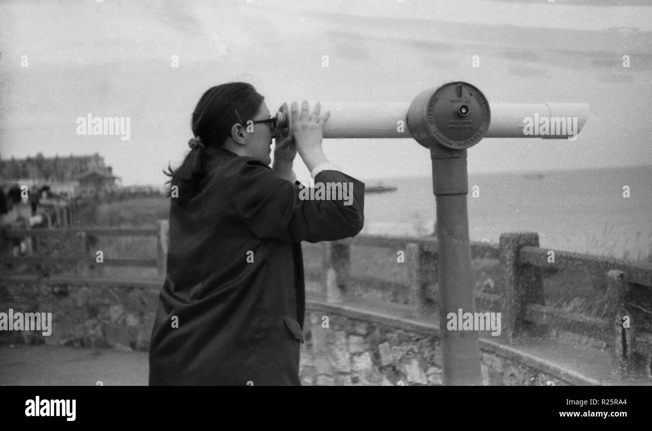 Margate, Kent, 1970, mujer mirando a través de un telescopio que funcionan con monedas o visor en lo alto de un acantilado en la costa de Kent. Foto de stock