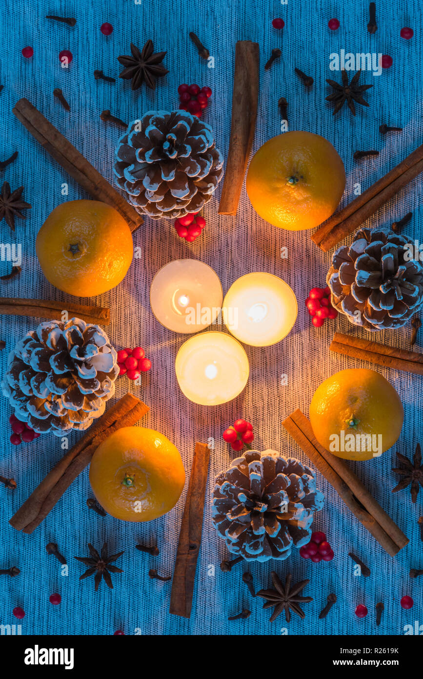 Navidad velas que brillan intensamente laicos plana rodeada por la corona de piñas, naranjas, canela, anís, clavo, bayas Foto de stock