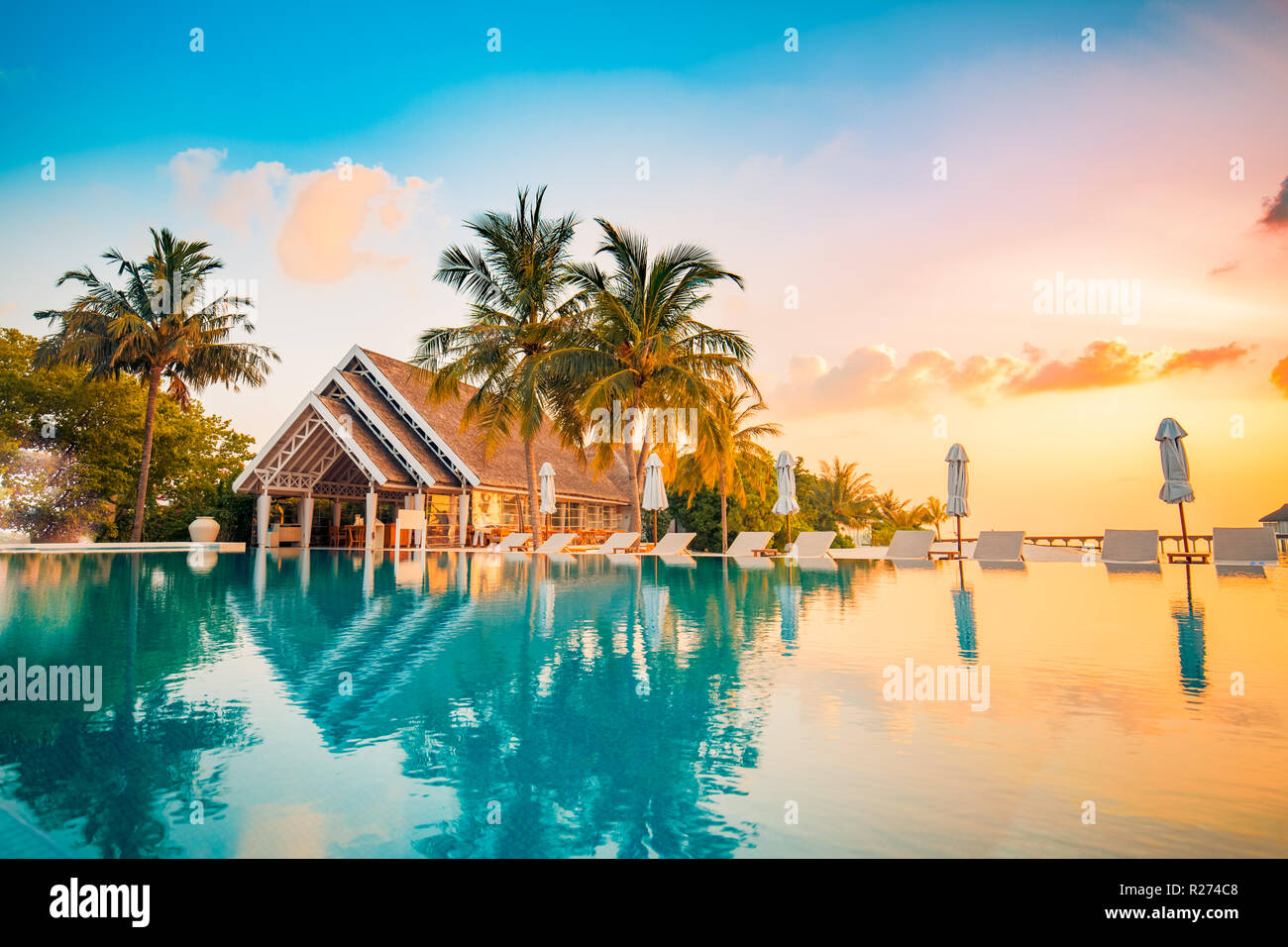 Hermosa piscina y sunset sky. Lujoso paisaje tropical en la playa, hamacas y tumbonas y el reflejo del agua. Foto de stock