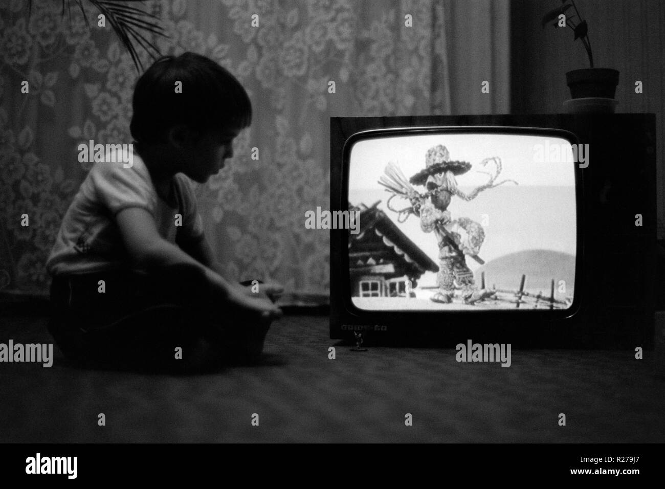 Joven sentado en el suelo viendo dibujos animados en un televisor Vintage 1970 Hungría Foto de stock