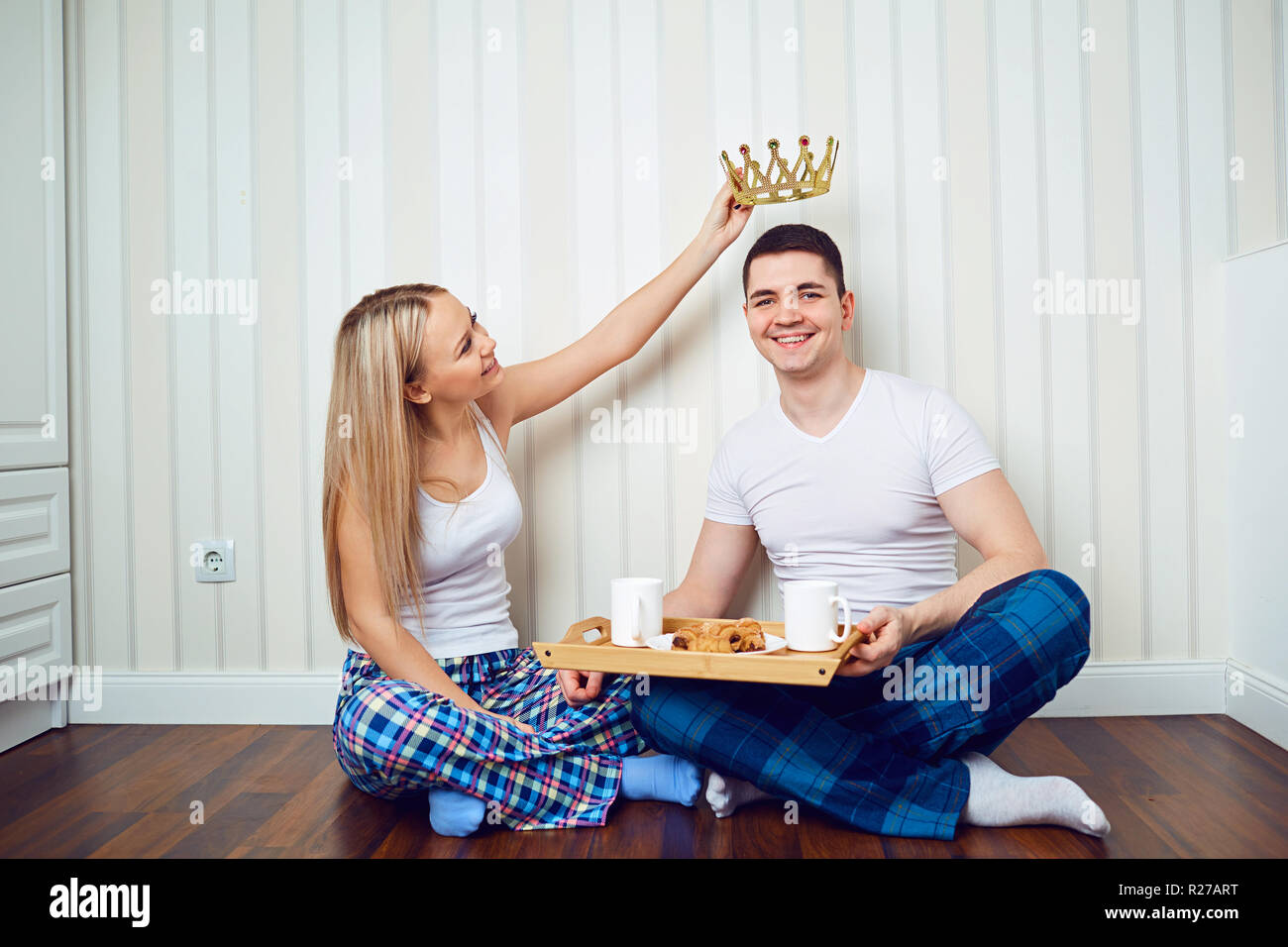 Una pareja feliz en pijama sentada en el piso de una habitación contra un Foto de stock