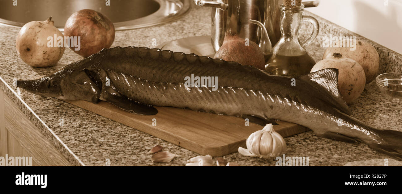 Esturión entera cruda acostado sobre la plancha de madera con granadas y  especias en mesa de piedra Fotografía de stock - Alamy