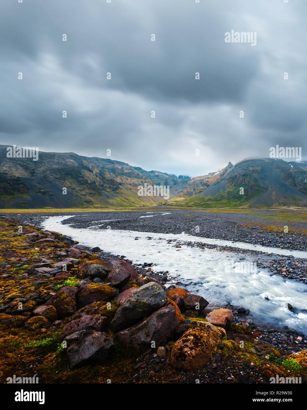 Islandia típico paisaje con Río y montañas. Cielo dramático y piedras rojas en primer plano Foto de stock