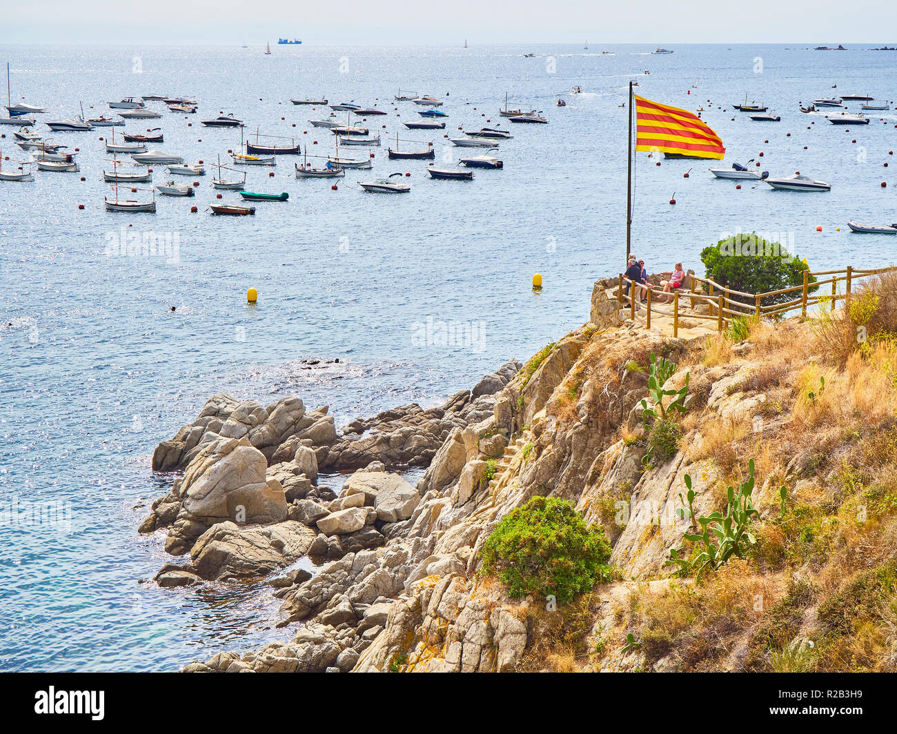 Los turistas que visitan Punta dels Burricaires viewpoint bajo la bandera oficial de Cataluña, llamada Senyera. Calella de Palafrugell, Girona, España Foto de stock