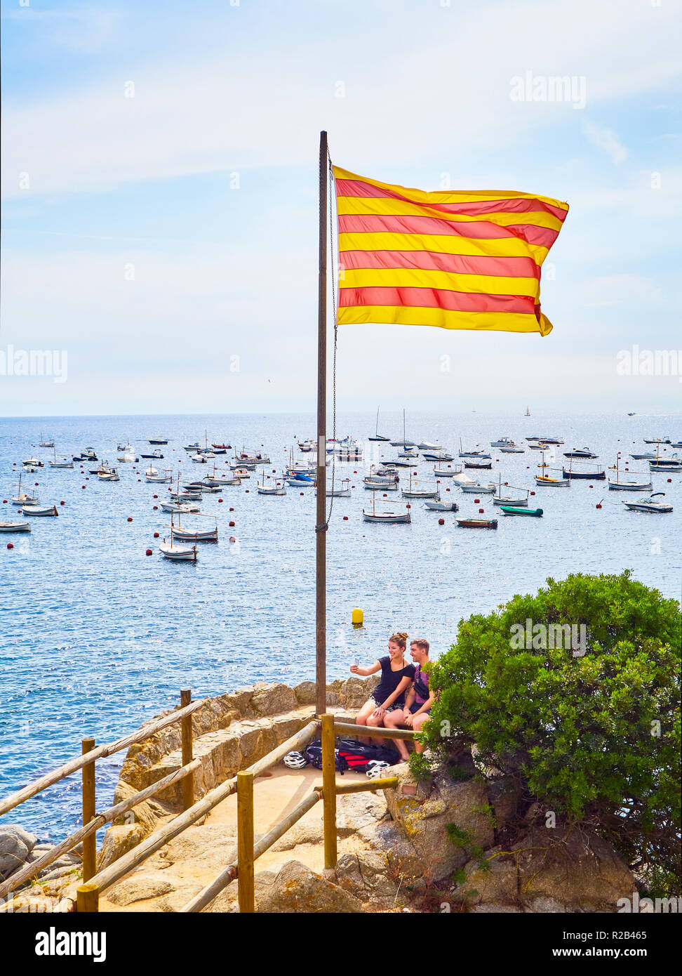 Una joven pareja de turistas tomando un selfie bajo la bandera oficial de Cataluña en Punta dels Burricaires de Calella de Palafrugell, Girona, España. Foto de stock