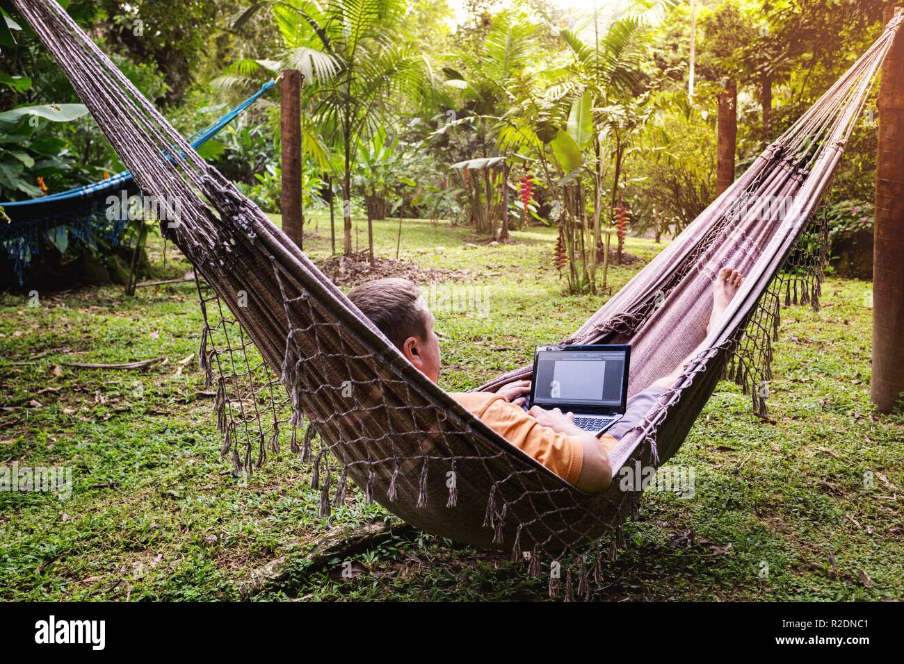 Hombre tumbado en una hamaca y trabajando en un portátil en el jardín  Fotografía de stock - Alamy