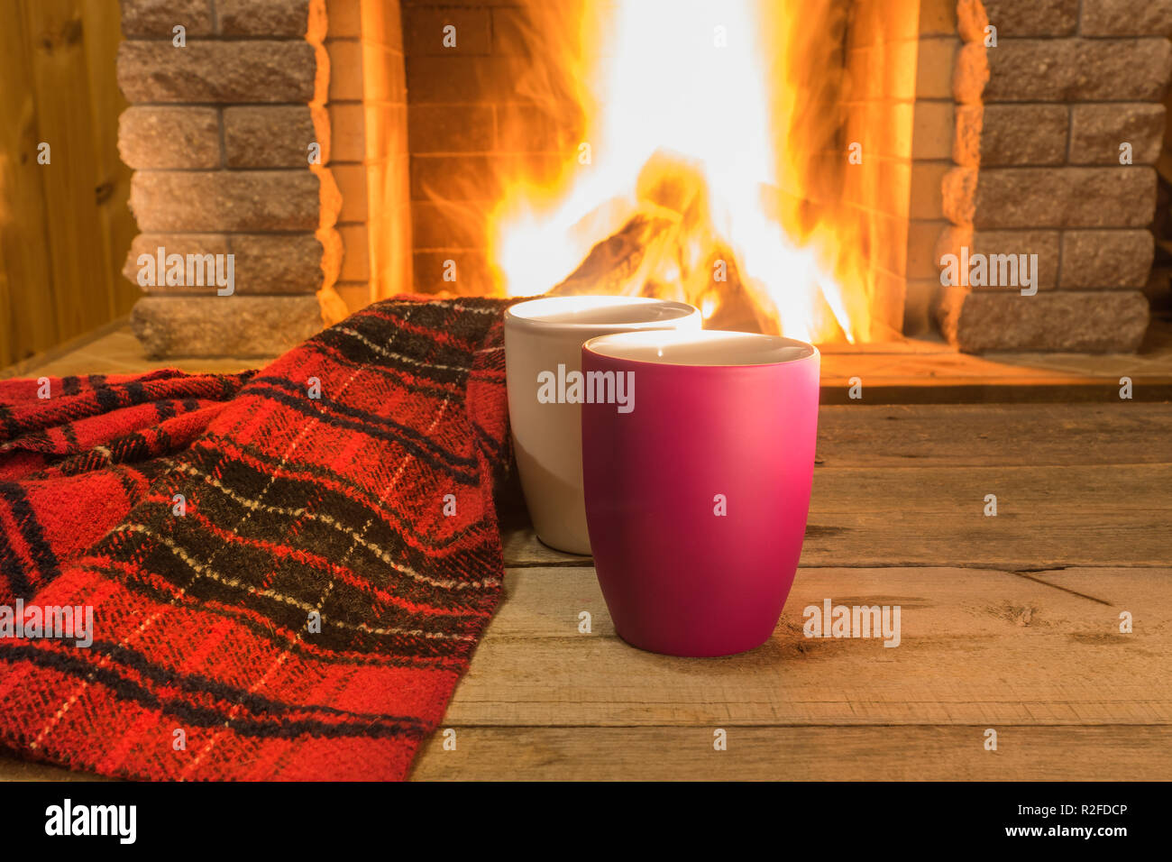 Dos tazas de té caliente y acogedor re caliente bufanda cerca de la chimenea, en casa de campo, vacaciones de invierno, en horizontal. Foto de stock