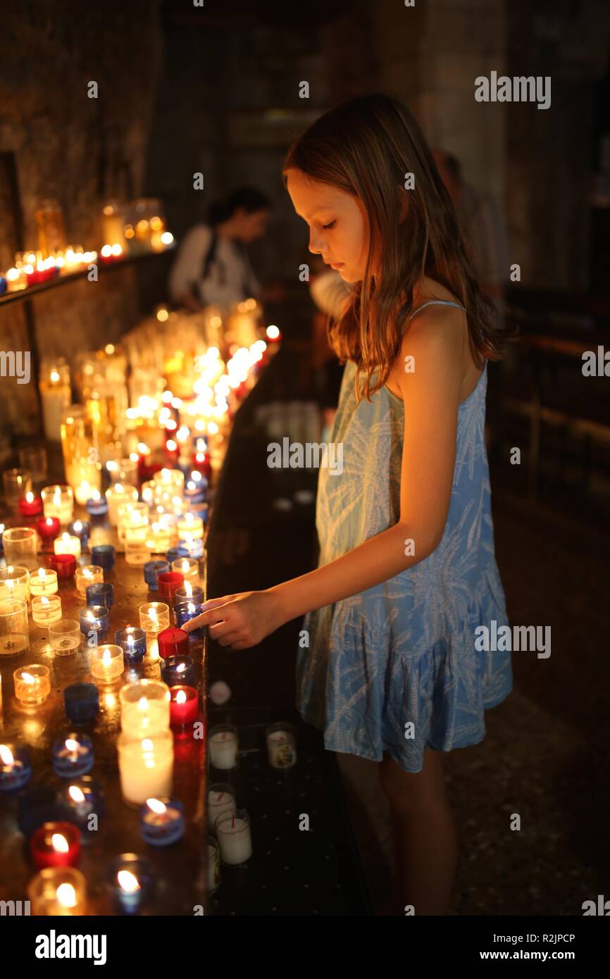 Chica colocando velas entre línea de velas en la iglesia católica Foto de stock