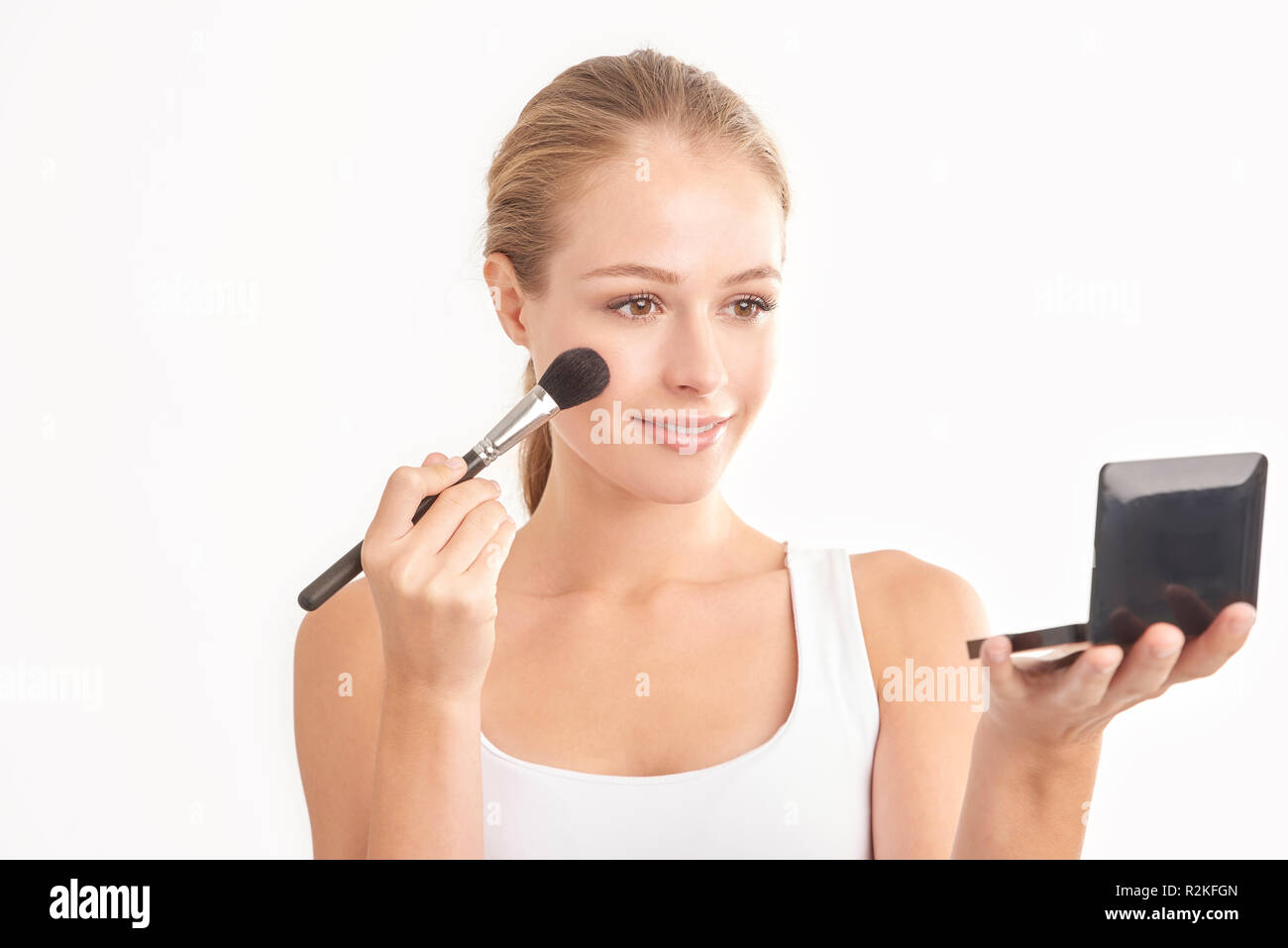 Foto de estudio cerca de la hermosa joven sosteniendo la mano y paleta de maquillaje pincel mientras la aplicación de maquillaje. Aislado sobre fondo blanco. Foto de stock