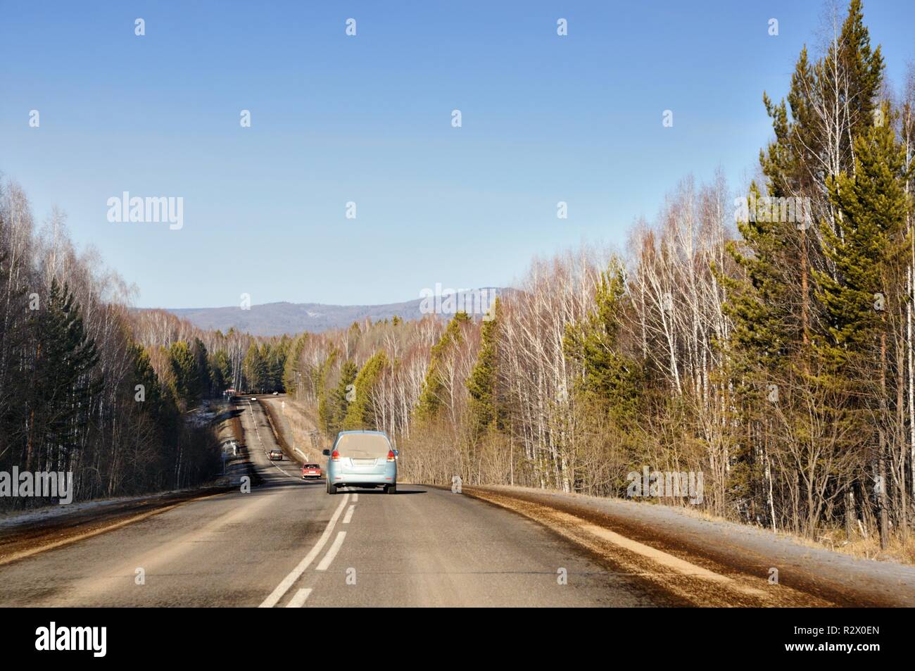 Paisaje otoñal con carretera de asfalto en las suaves colinas cubiertas de bosques de taiga bajo un cielo azul en Siberia, Rusia Foto de stock