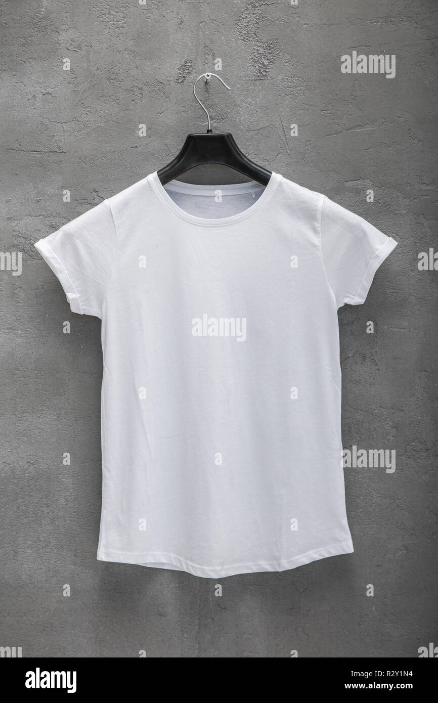 El lado delantero de la mujer blanca camiseta de algodón en una percha y un  muro de hormigón en el fondo. T-shirt sin imprimir Fotografía de stock -  Alamy