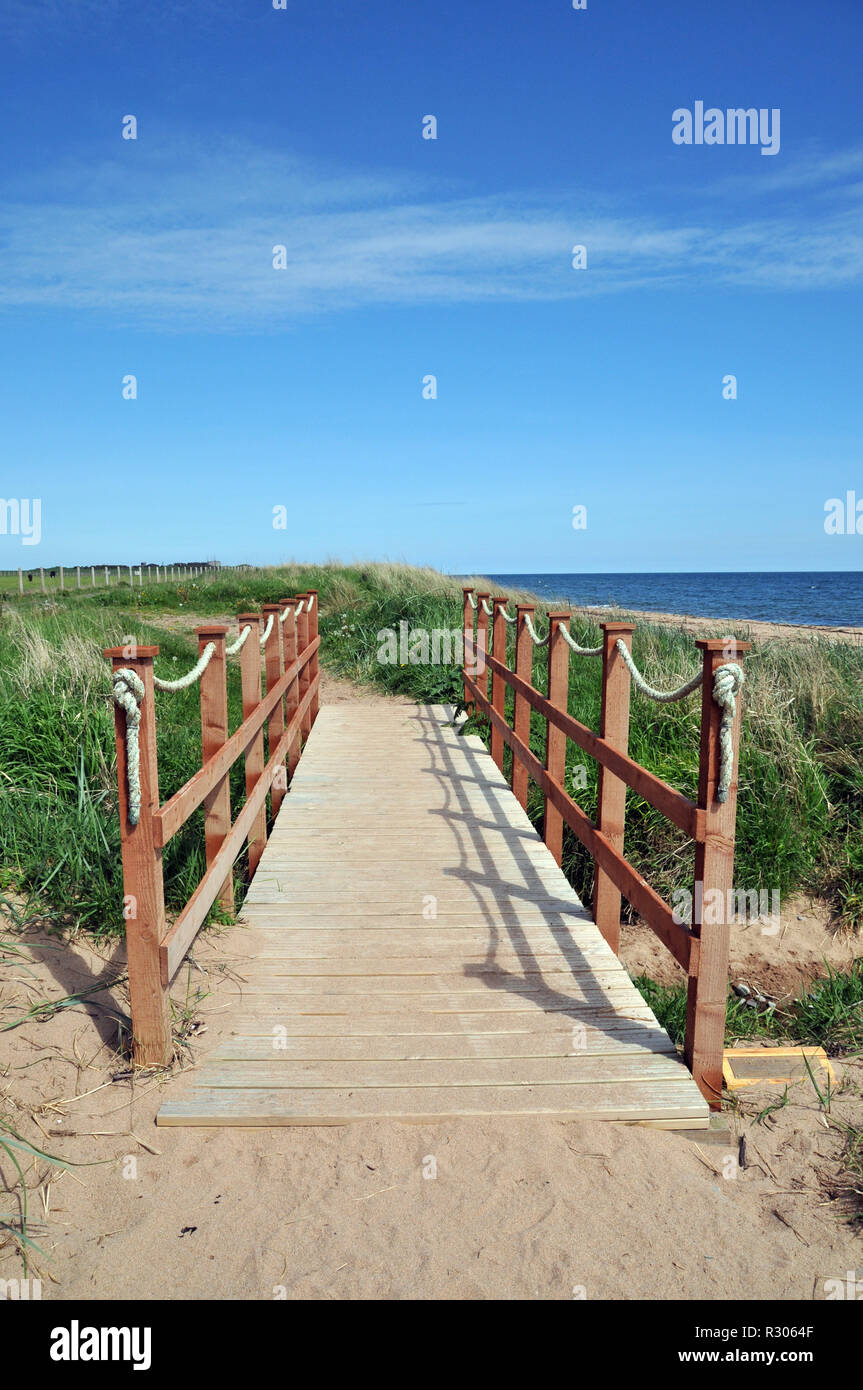 Puente de madera para caminantes que abarca un pequeño estuario en la costa. Foto de stock
