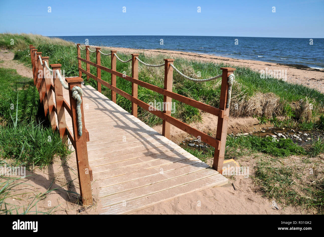 Puente de madera para caminantes que abarca un pequeño estuario en la costa. Foto de stock