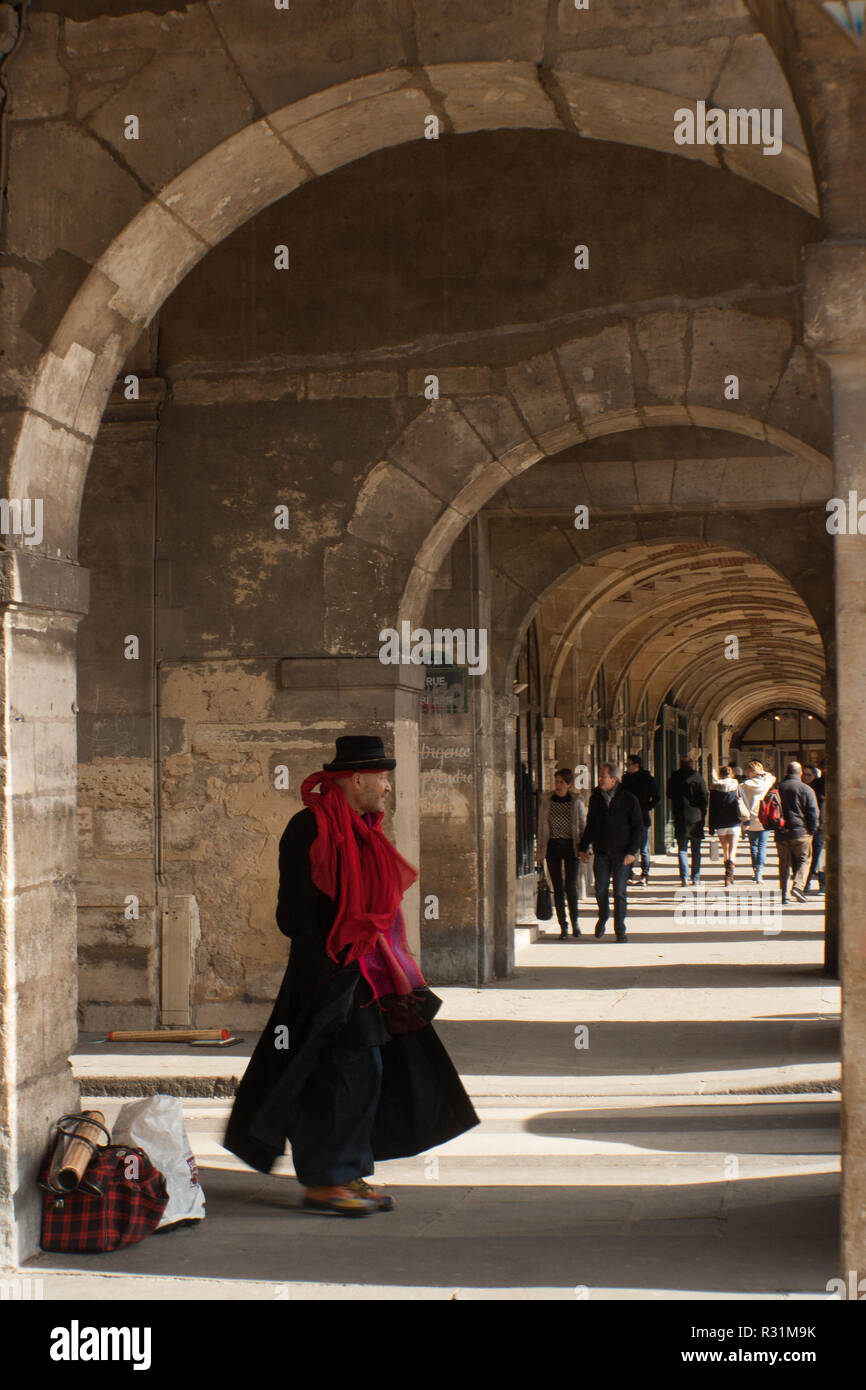 Artista callejero en Le Marais, París, pararse bajo arcos de piedra, arcade, vistiendo ropa negra y sombrero y un pañuelo rojo. Punto de fuga Foto de stock
