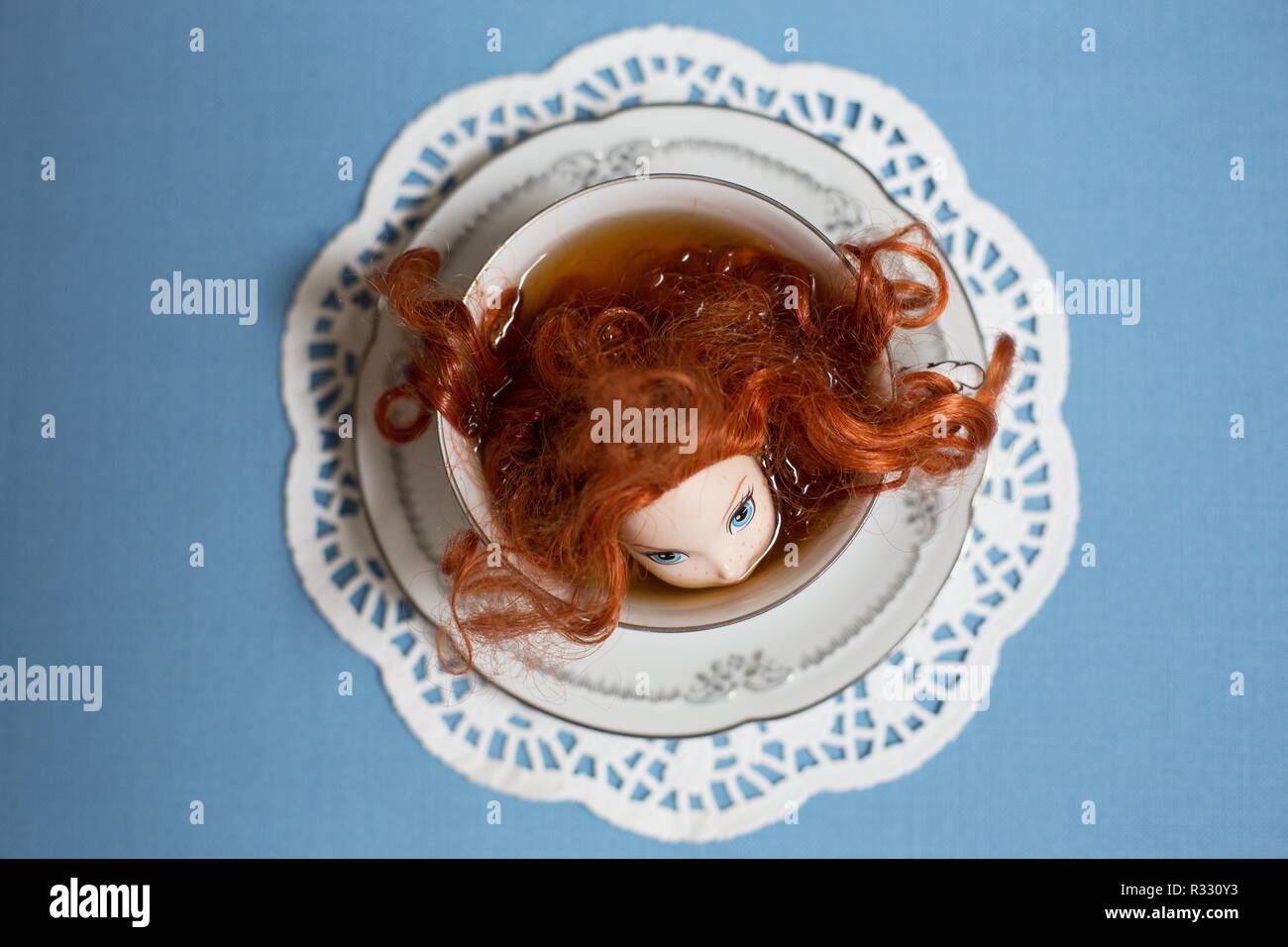 Imagen surrealista de muñeca de cabeza roja en una taza de té. Foto de stock