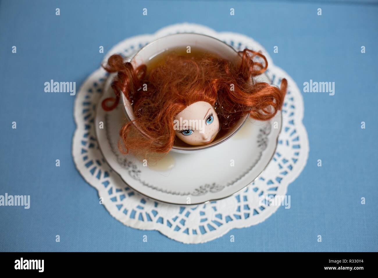Imagen surrealista de muñeca de cabeza roja en una taza de té. Foto de stock