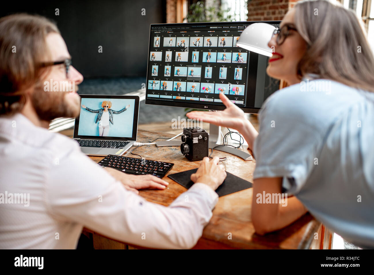 Pareja joven de fotógrafos que trabajan con retratos de la mujer en el lugar de trabajo con dos ordenadores en el studio Foto de stock