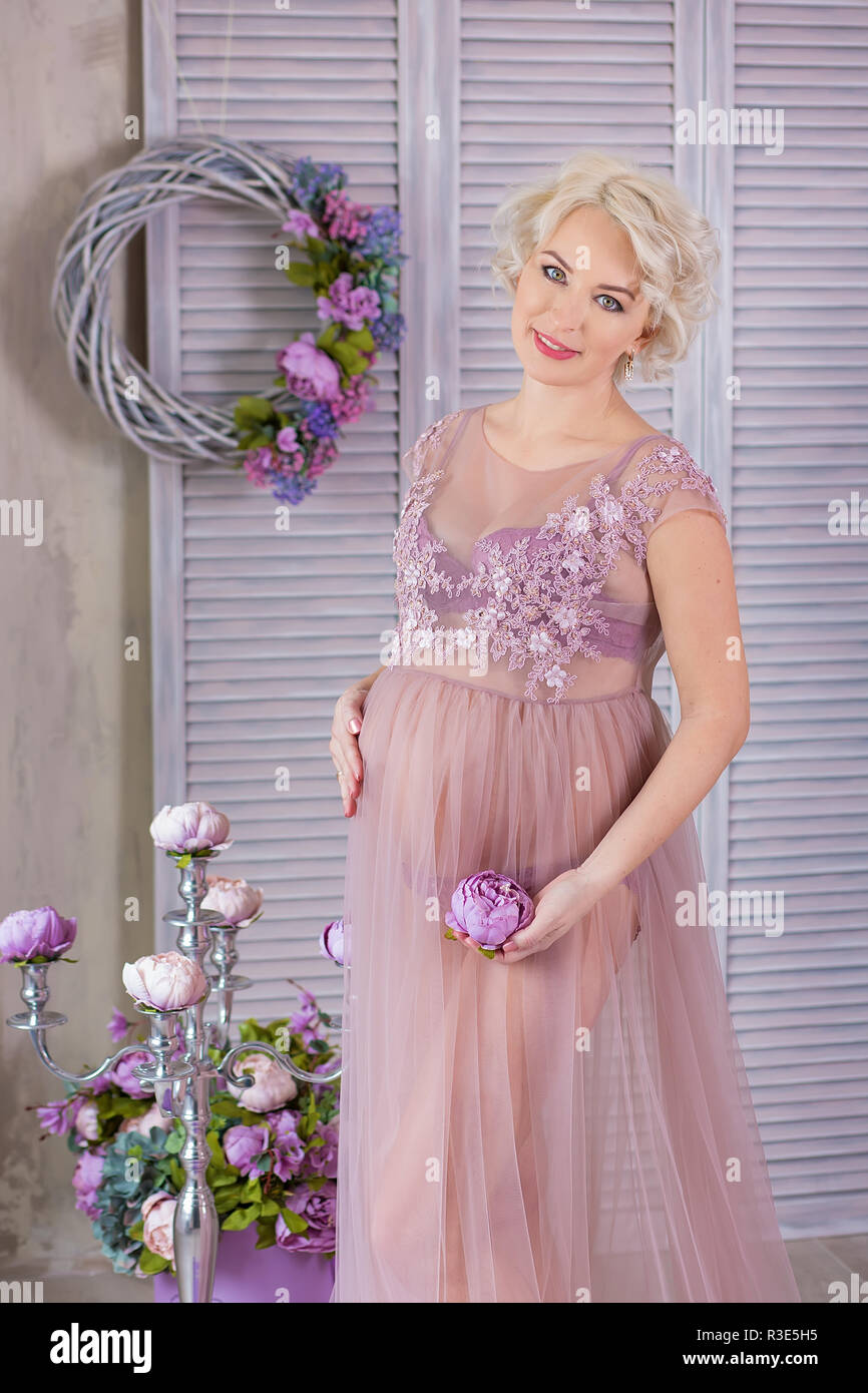 El embarazo, la maternidad y la feliz futura madre gestante en concepto -  Vestido violeta ventilado con ramo de flores contra la pared colorida  posando con SIL Fotografía de stock - Alamy