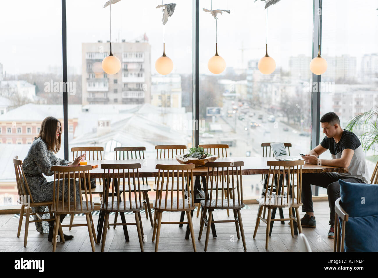 Dos personas, un hombre joven y una mujer sentada a una mesa grande, desde diferentes lados. Distancia entre las personas. El concepto moderno de comunicaciones personales problema Foto de stock