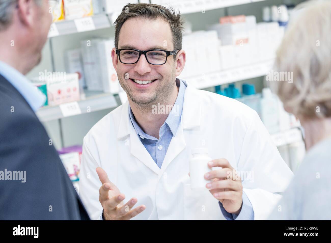 Macho sonriente farmacéutico explicar la medicación para los clientes superiores en farmacia. Foto de stock