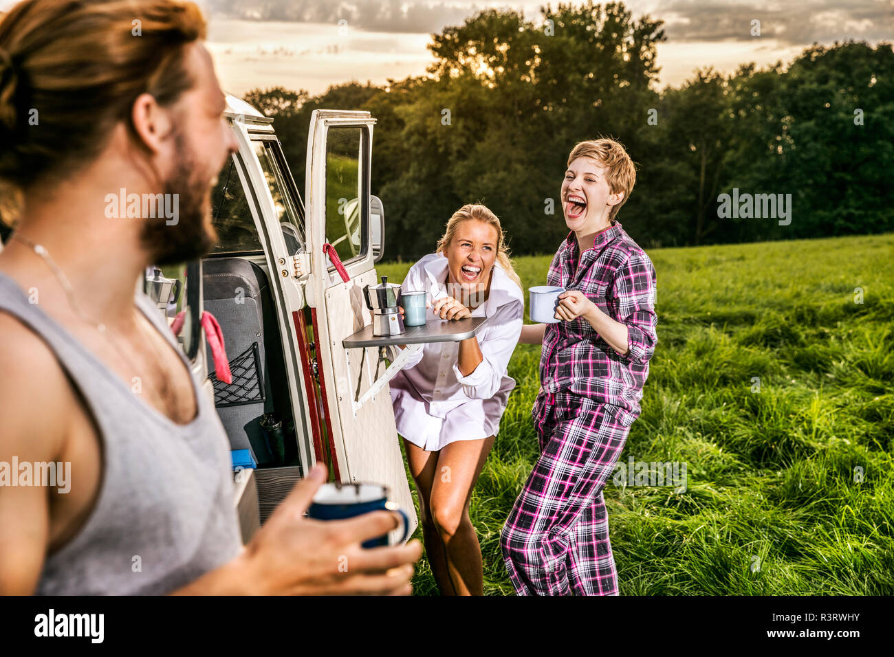 Despreocupados amigos disfrutando de café en una furgoneta en paisaje rural Foto de stock