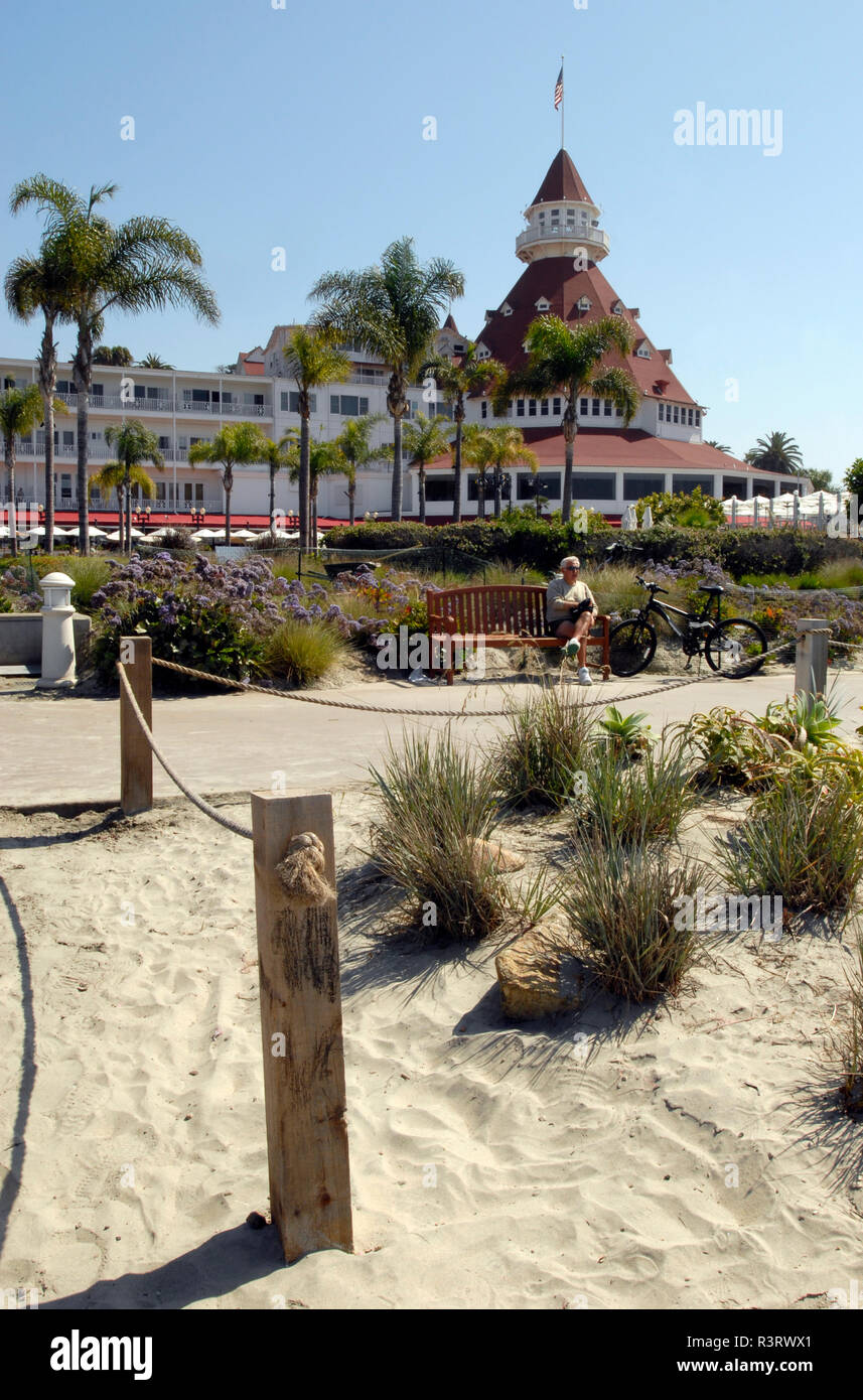 Un ciclista descanse por un camino cerca del histórico Hotel del Coronado, cerca de San Diego, California. El Landmark Victorian beach resort abrió sus puertas en 1888. Foto de stock