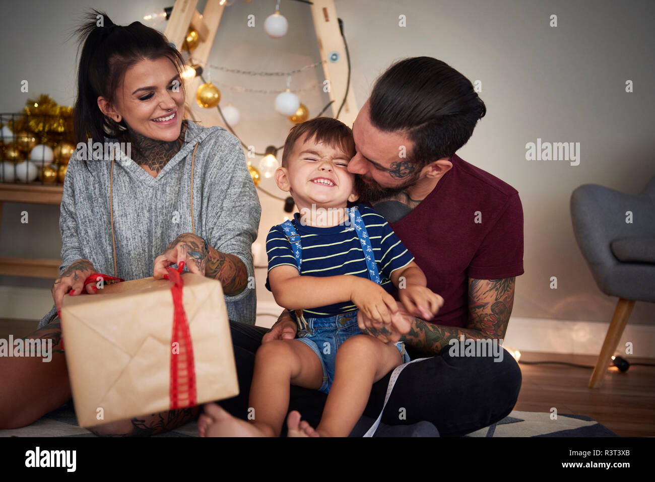 Muchacho feliz abriendo regalo de Navidad con sus padres en casa Foto de stock