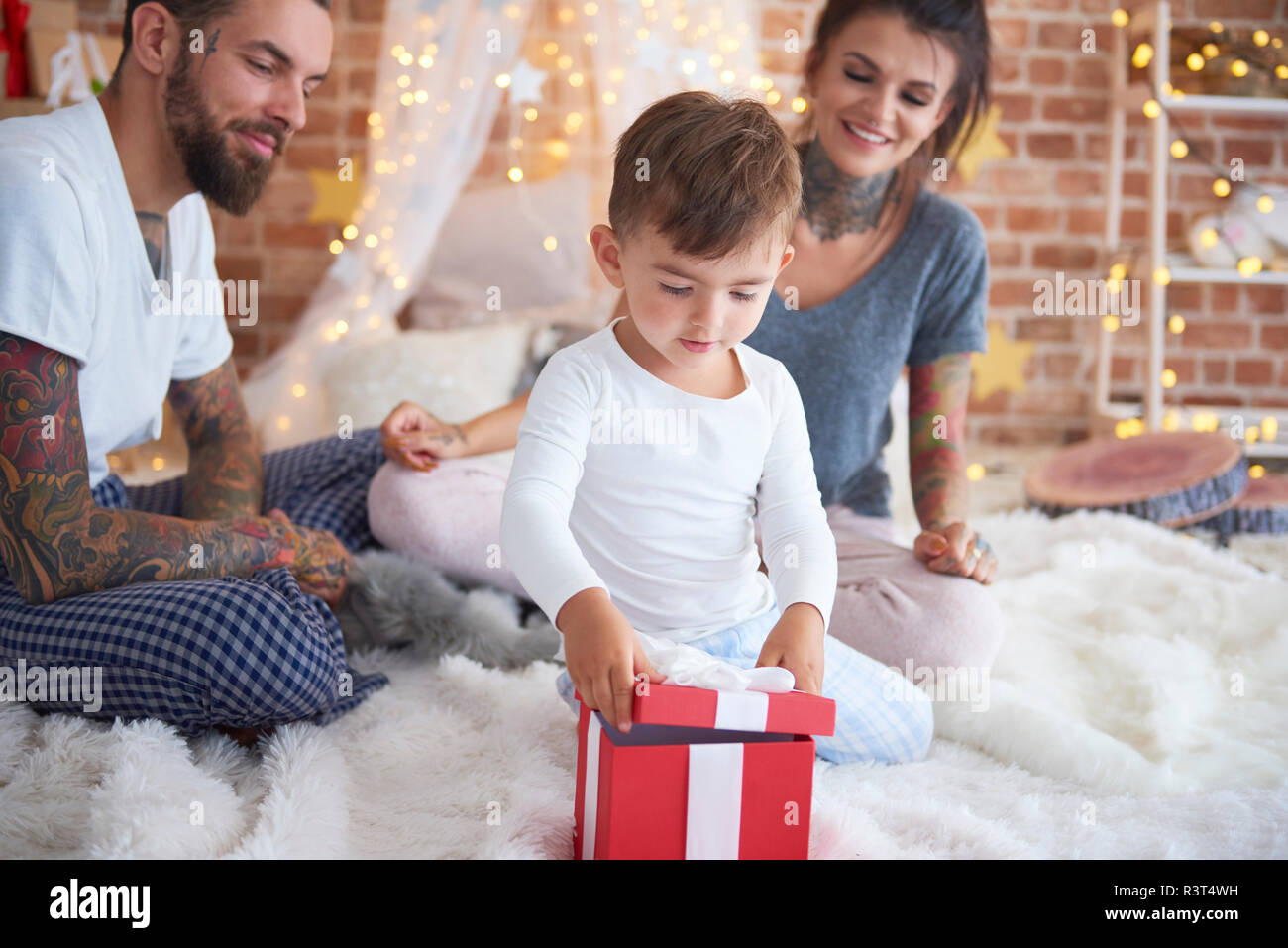 Niño abriendo regalo de Navidad con sus padres en la cama Foto de stock