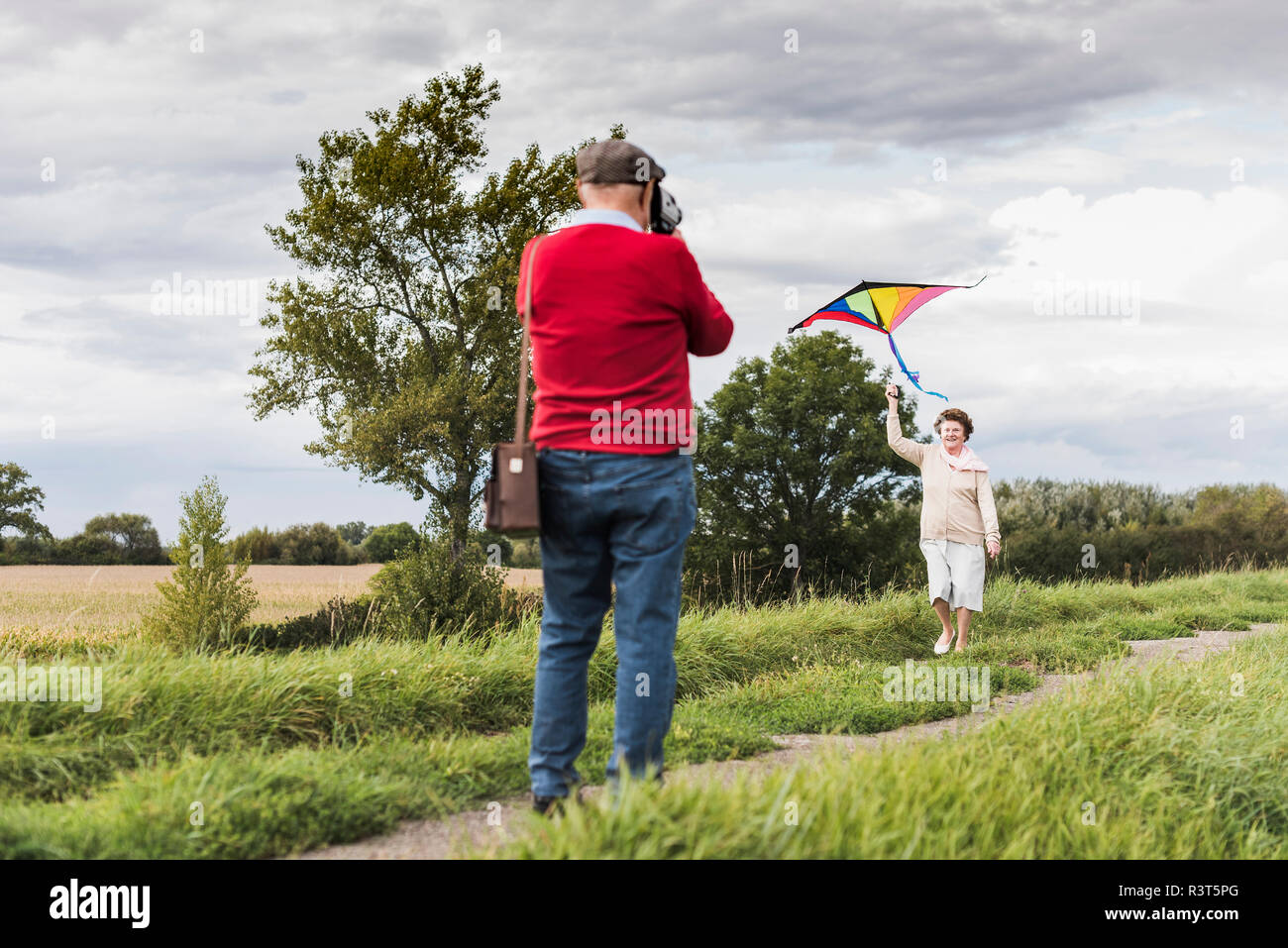 Hombre Senior filmando esposa volar cometa en paisaje rural Foto de stock