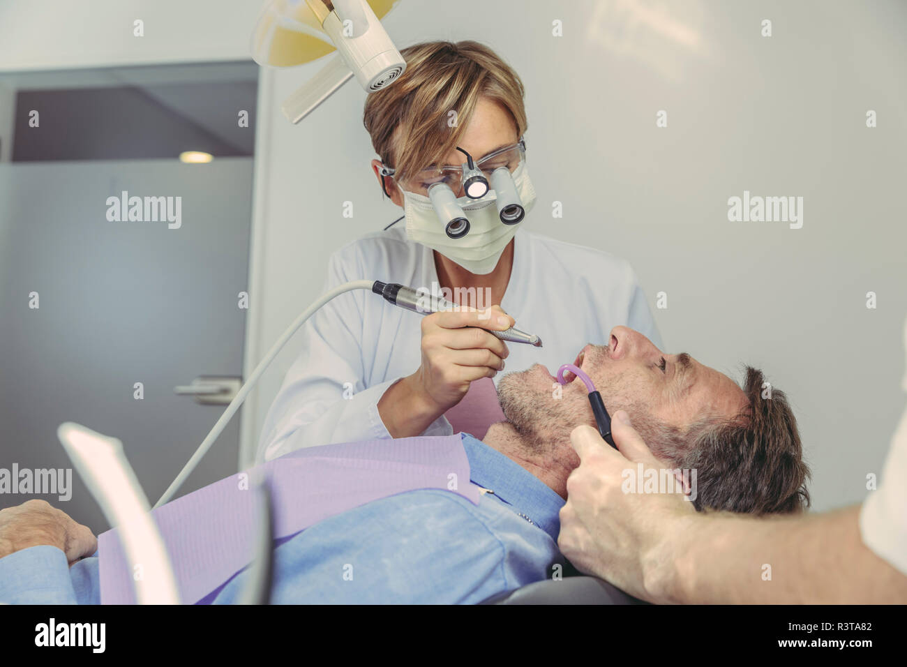 Paciente recibiendo tratamiento dental, dentista con taladro dental y lupas de cabeza y luz Foto de stock